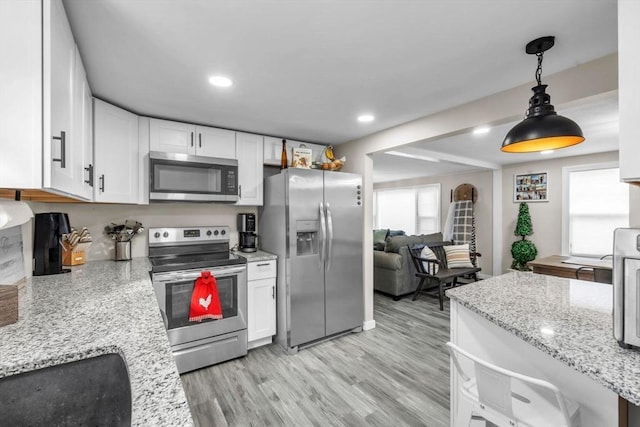 kitchen featuring white cabinets, hanging light fixtures, light hardwood / wood-style floors, stainless steel appliances, and light stone countertops