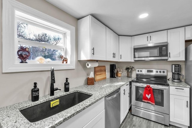 kitchen with sink, light stone countertops, white cabinets, and appliances with stainless steel finishes