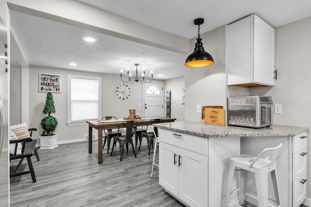 kitchen with pendant lighting, white cabinetry, a breakfast bar area, light stone counters, and light wood-type flooring