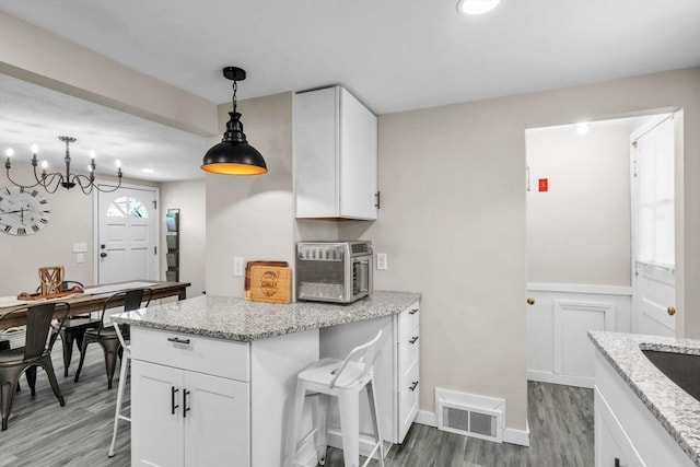 kitchen featuring light stone countertops, a breakfast bar area, white cabinets, and decorative light fixtures