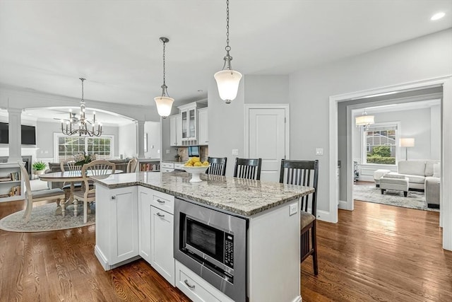 4 Fairfield Pl, Winchester, MA 01890 - kitchen with decorative columns, stainless steel microwave, a kitchen breakfast bar, dark wood finished floors, and light stone counters