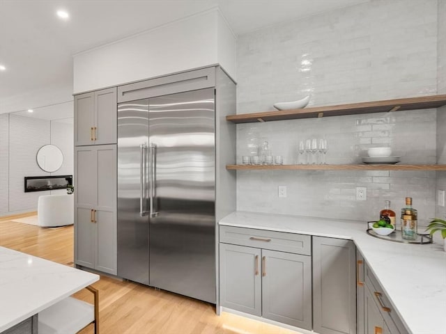 kitchen with gray cabinetry, stainless steel built in refrigerator, a sink, decorative backsplash, and light wood-style floors