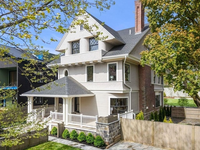 victorian house with covered porch, fence, a shingled roof, and a chimney