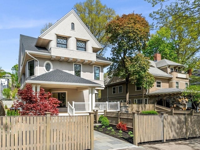 view of front of home with a fenced front yard, a porch, and roof with shingles