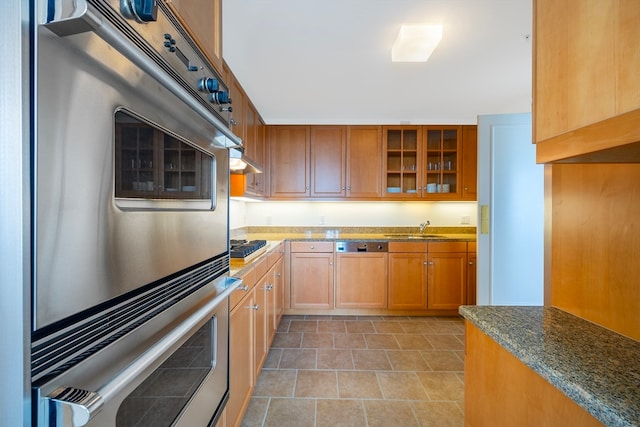 kitchen featuring dark stone countertops, stainless steel double oven, black gas cooktop, and sink