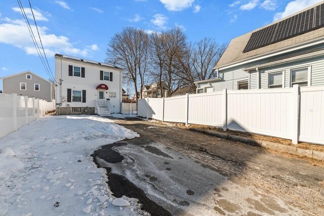 rear view of house with entry steps, a fenced backyard, a shingled roof, and solar panels