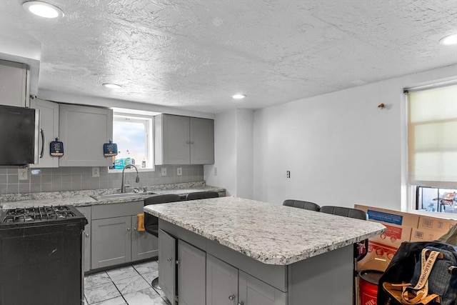 kitchen featuring tasteful backsplash, marble finish floor, gray cabinetry, a sink, and gas stove