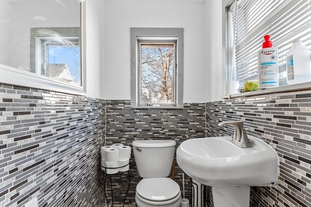 half bath with toilet, tile walls, and a sink