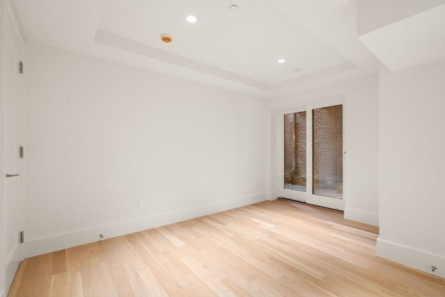 empty room with recessed lighting, a raised ceiling, baseboards, and light wood finished floors