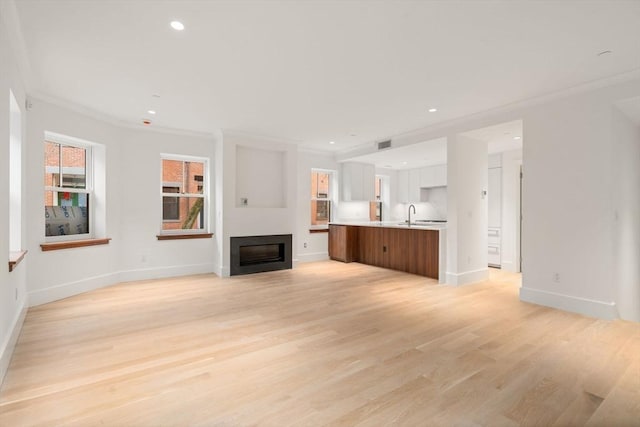 unfurnished living room with light wood-type flooring, a sink, crown molding, and recessed lighting