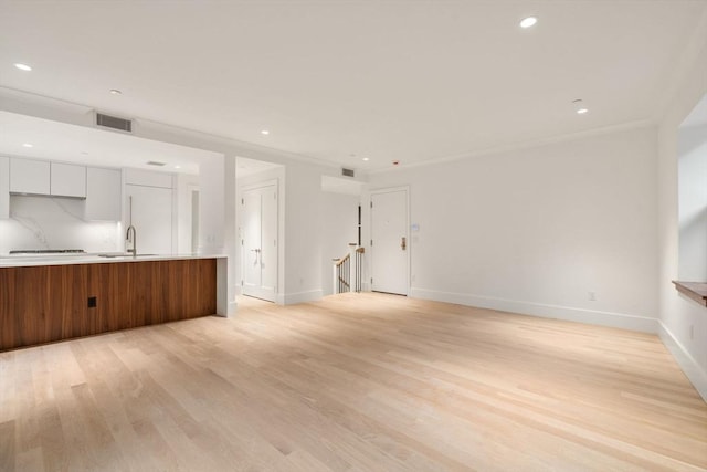 unfurnished living room with recessed lighting, visible vents, light wood-style flooring, a sink, and baseboards