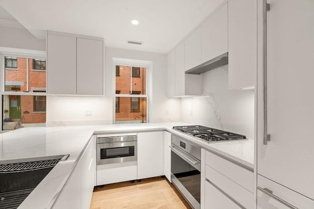 kitchen featuring visible vents, white cabinets, light stone counters, stainless steel appliances, and light wood-type flooring