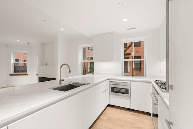 kitchen with light wood-type flooring, white cabinetry, a sink, and oven