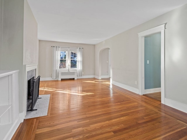 unfurnished living room featuring a fireplace, radiator heating unit, and hardwood / wood-style floors