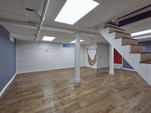 basement featuring wooden walls, a drop ceiling, and dark hardwood / wood-style floors