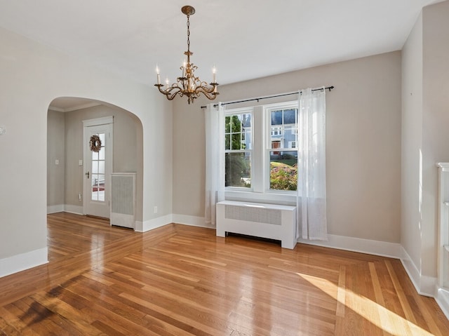 empty room with light wood-type flooring, radiator heating unit, and an inviting chandelier