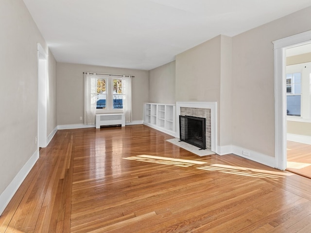 unfurnished living room featuring hardwood / wood-style floors, radiator heating unit, and a brick fireplace