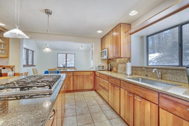 kitchen featuring pendant lighting, light tile patterned floors, appliances with stainless steel finishes, a sink, and light stone countertops