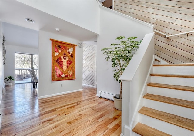 stairway with a baseboard radiator, visible vents, baseboards, and wood finished floors