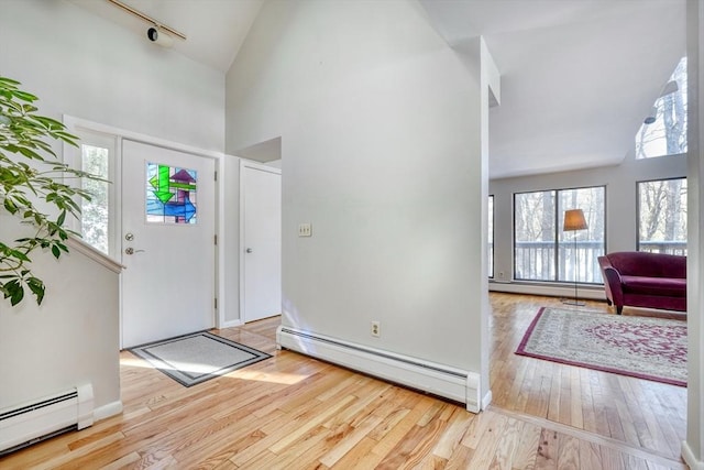 foyer featuring light wood-type flooring, high vaulted ceiling, a baseboard heating unit, and track lighting