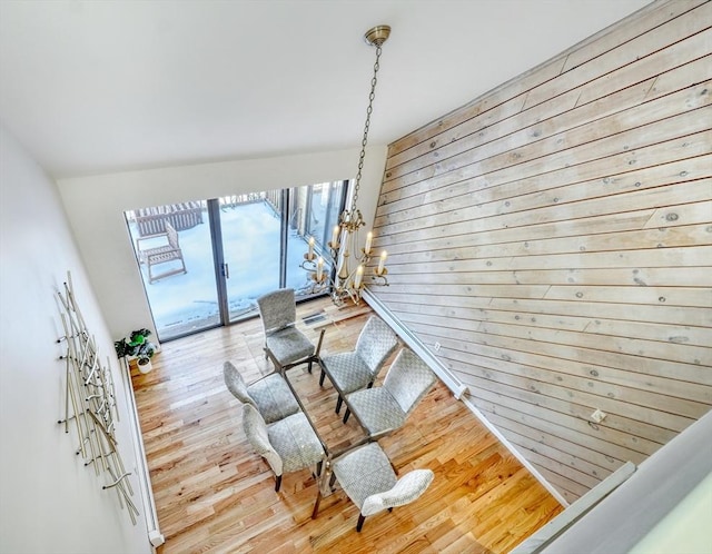 dining room featuring light wood-type flooring, wooden walls, and a notable chandelier