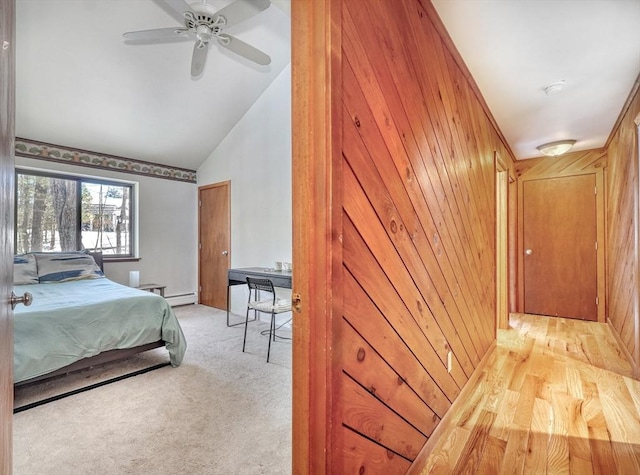 bedroom with a baseboard radiator, light carpet, vaulted ceiling, wooden walls, and ceiling fan