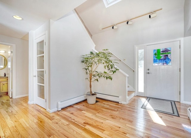 entryway with a baseboard radiator, baseboards, stairs, light wood-type flooring, and rail lighting