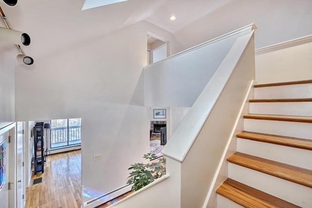 staircase with a baseboard heating unit, a skylight, wood finished floors, and recessed lighting