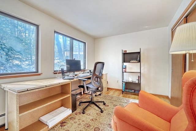 office area featuring a baseboard heating unit, light wood finished floors, and baseboards