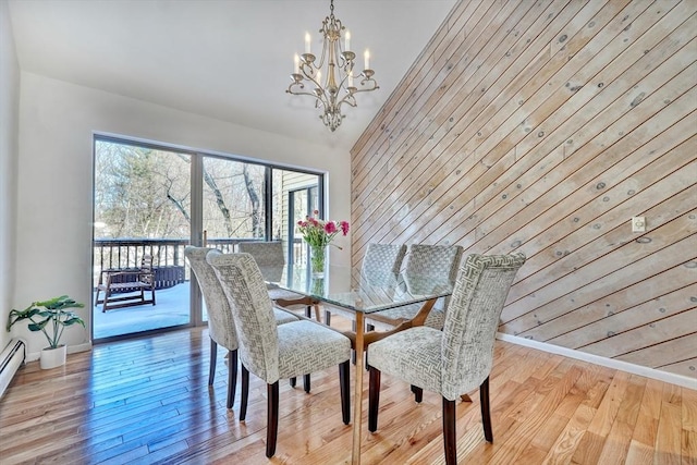 dining room with light wood-style flooring, an inviting chandelier, vaulted ceiling, wood walls, and baseboards