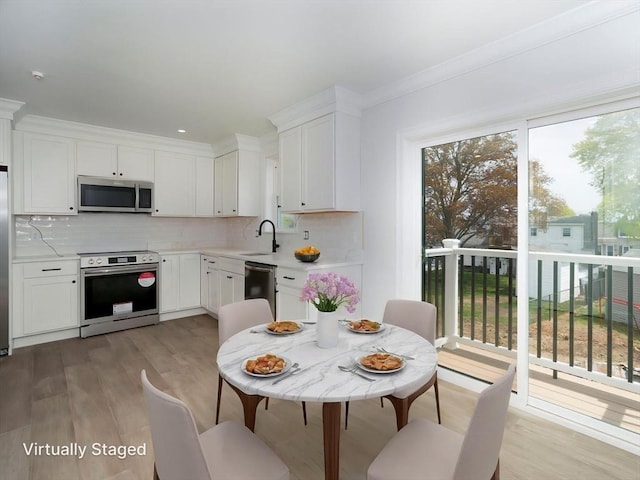 kitchen featuring appliances with stainless steel finishes, a sink, light countertops, light wood-style flooring, and tasteful backsplash