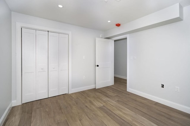 unfurnished bedroom with baseboards, recessed lighting, wood finished floors, and a closet
