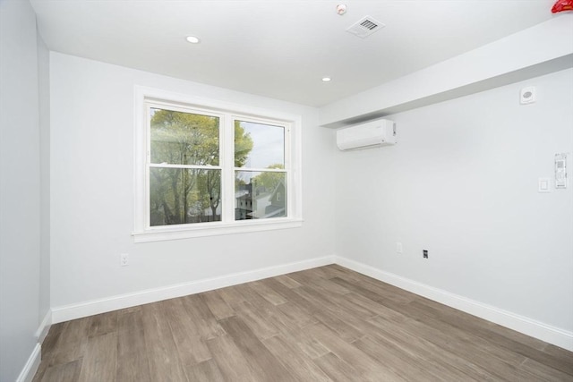 empty room with visible vents, a wall mounted air conditioner, baseboards, and wood finished floors