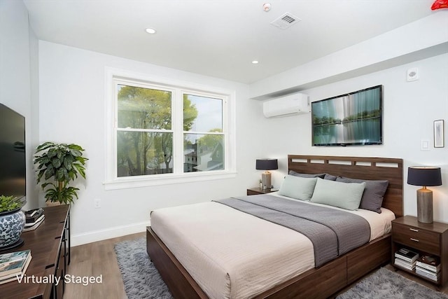 bedroom featuring visible vents, wood finished floors, baseboards, an AC wall unit, and recessed lighting