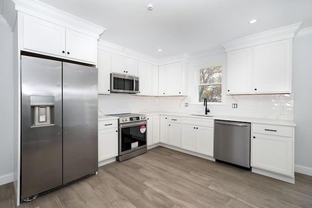 kitchen featuring white cabinets, appliances with stainless steel finishes, a sink, light wood-style floors, and light countertops