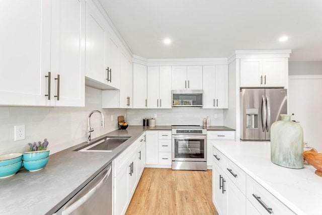 kitchen featuring sink, white cabinetry, light wood-type flooring, appliances with stainless steel finishes, and decorative backsplash