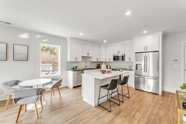 kitchen with a kitchen island, appliances with stainless steel finishes, tasteful backsplash, a breakfast bar area, and white cabinets