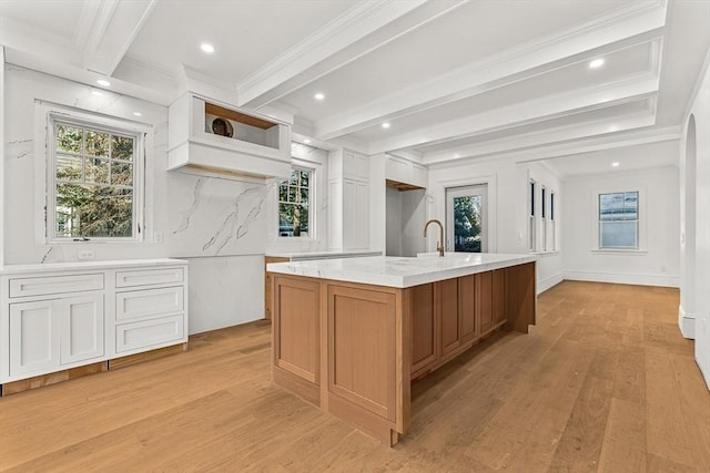 kitchen with a spacious island, white cabinetry, crown molding, light wood-type flooring, and beamed ceiling