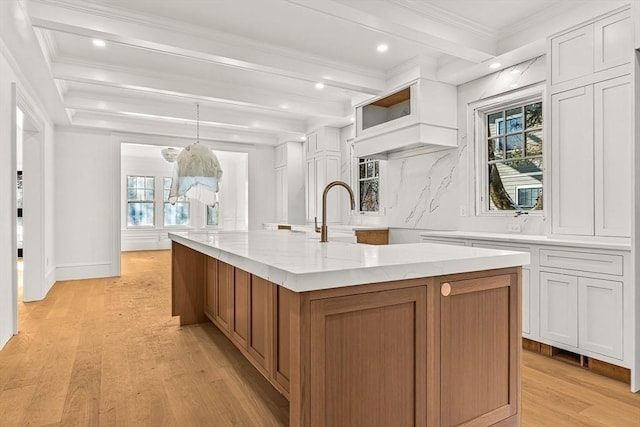 kitchen featuring pendant lighting, beamed ceiling, white cabinets, light stone counters, and a spacious island