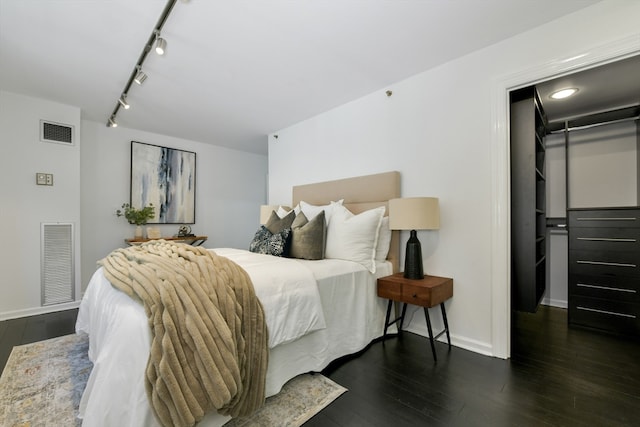 bedroom with track lighting, a closet, dark hardwood / wood-style flooring, and a walk in closet