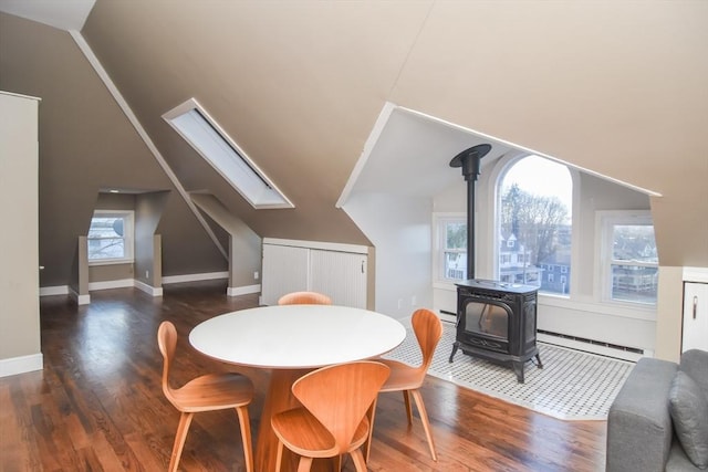 dining area with a wood stove, lofted ceiling with skylight, dark hardwood / wood-style flooring, and a baseboard heating unit