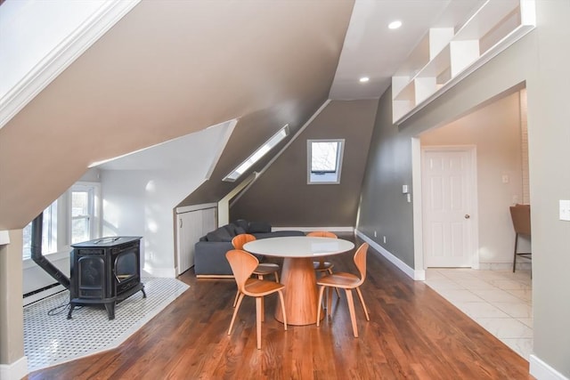 dining room featuring a wood stove, vaulted ceiling with skylight, and wood-type flooring