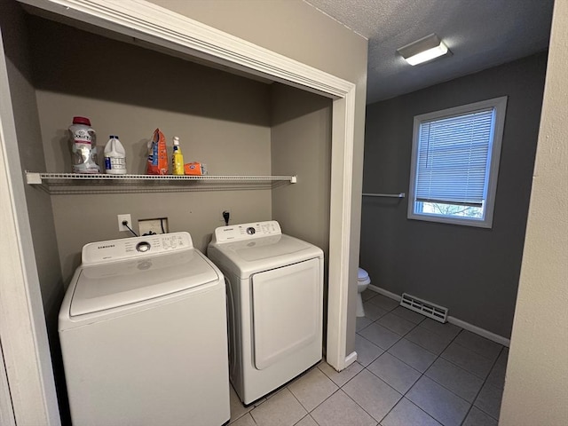 washroom with visible vents, washer and dryer, baseboards, a textured ceiling, and tile patterned floors