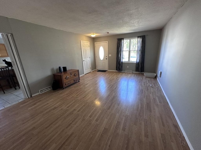 entryway with baseboards, a textured ceiling, visible vents, and wood finished floors