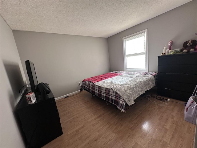 bedroom featuring a textured ceiling, baseboards, and light wood-style flooring