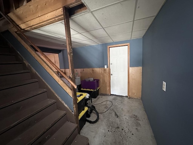 below grade area with stairway, wainscoting, wooden walls, and a paneled ceiling