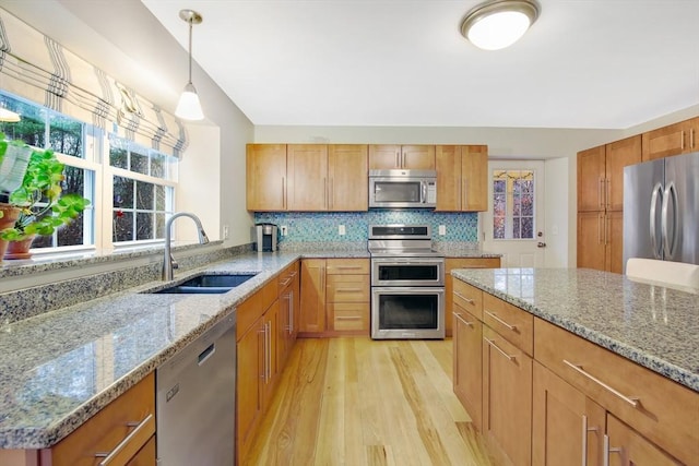 kitchen with light stone countertops, sink, pendant lighting, appliances with stainless steel finishes, and light wood-type flooring