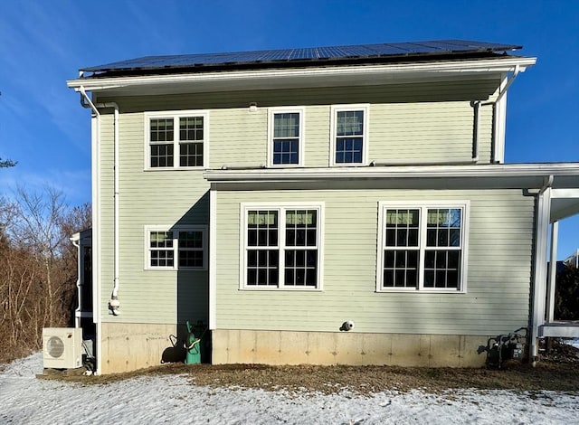 snow covered back of property featuring ac unit and solar panels