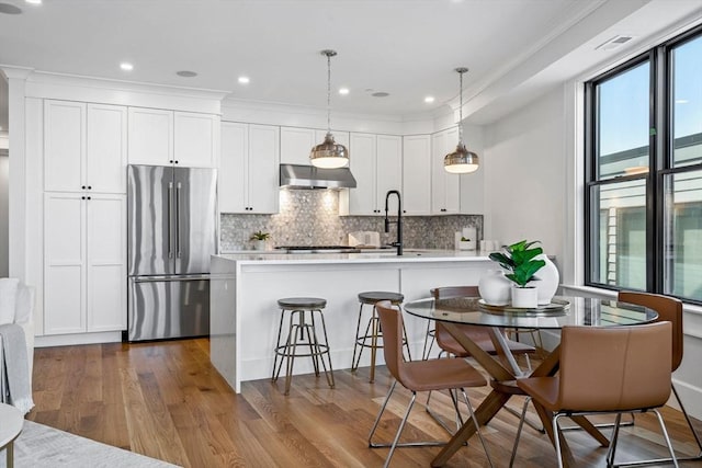 kitchen with high end fridge, under cabinet range hood, backsplash, dark wood finished floors, and white cabinetry