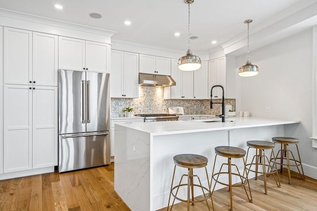 kitchen featuring under cabinet range hood, a kitchen breakfast bar, backsplash, high quality fridge, and a peninsula